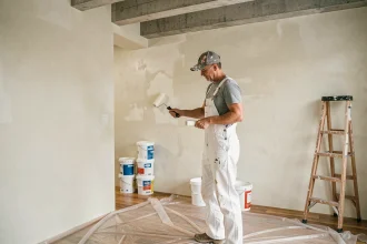 Peintre professionnel appliquant de la peinture blanche au rouleau dans une pièce en cours de rénovation avec des pots de peinture au sol