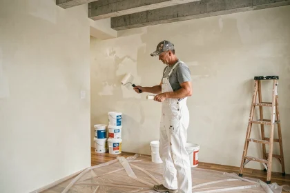 Peintre professionnel appliquant de la peinture blanche au rouleau dans une pièce en cours de rénovation avec des pots de peinture au sol